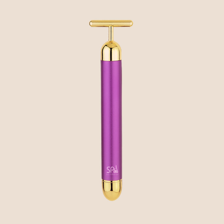 Michael Todd Beauty's Gold Bar facial massage tool features a T-shaped handle with purple and gold accents, set against a beige background.