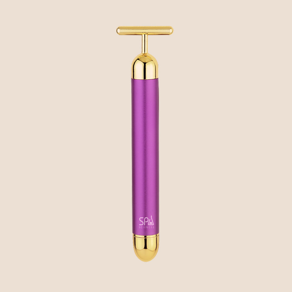 Michael Todd Beauty's Gold Bar facial massage tool features a T-shaped handle with purple and gold accents, set against a beige background.