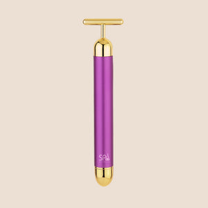 Michael Todd Beauty's Gold Bar facial massage tool features a T-shaped handle with purple and gold accents, set against a beige background.