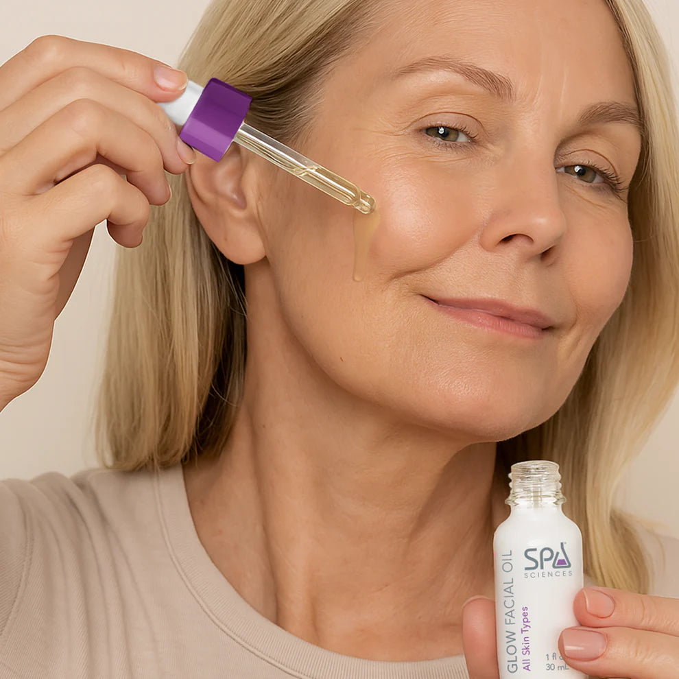 A woman applies facial oil to her cheek using a dropper, holding a bottle labeled