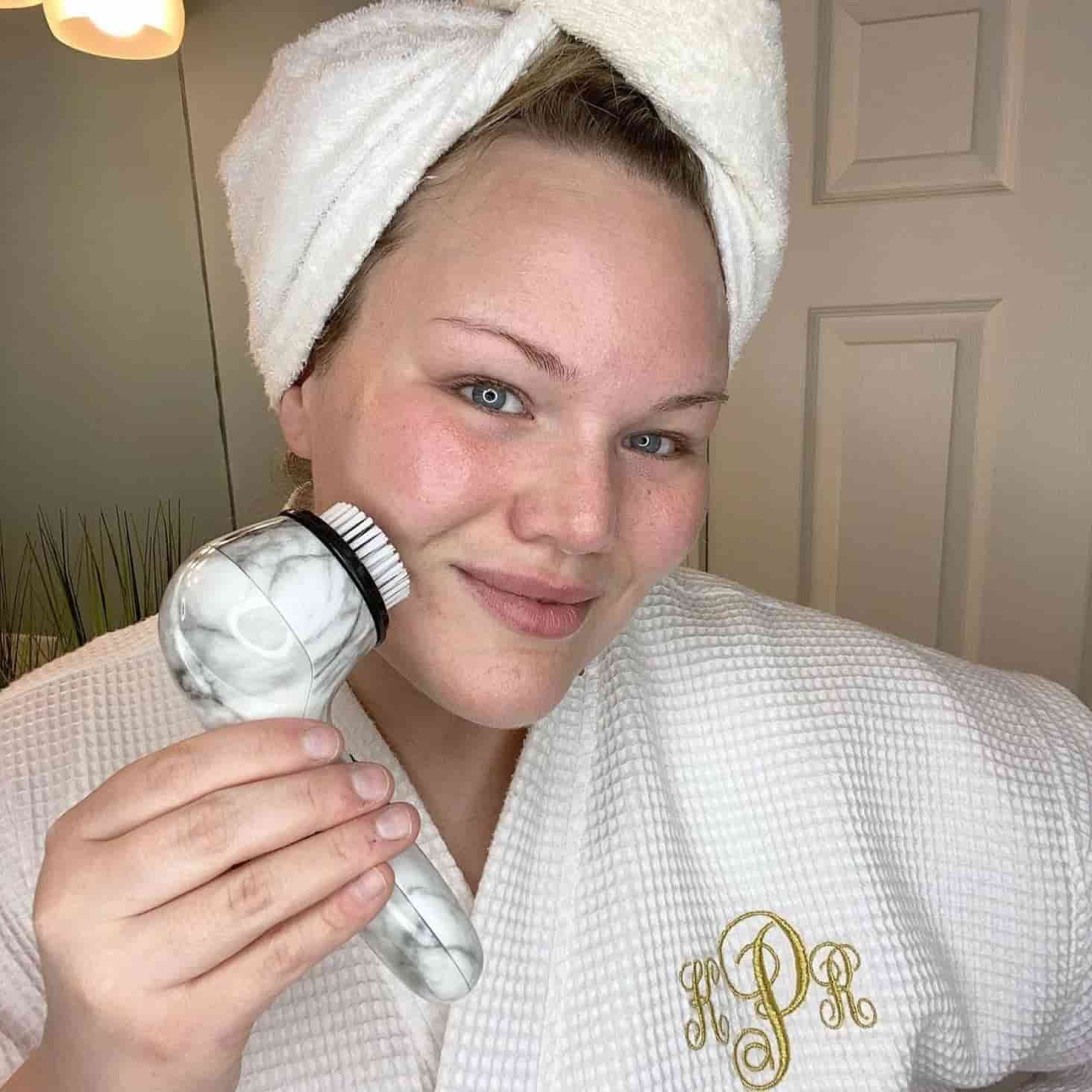 A woman in a towel holding an electric facial brush.