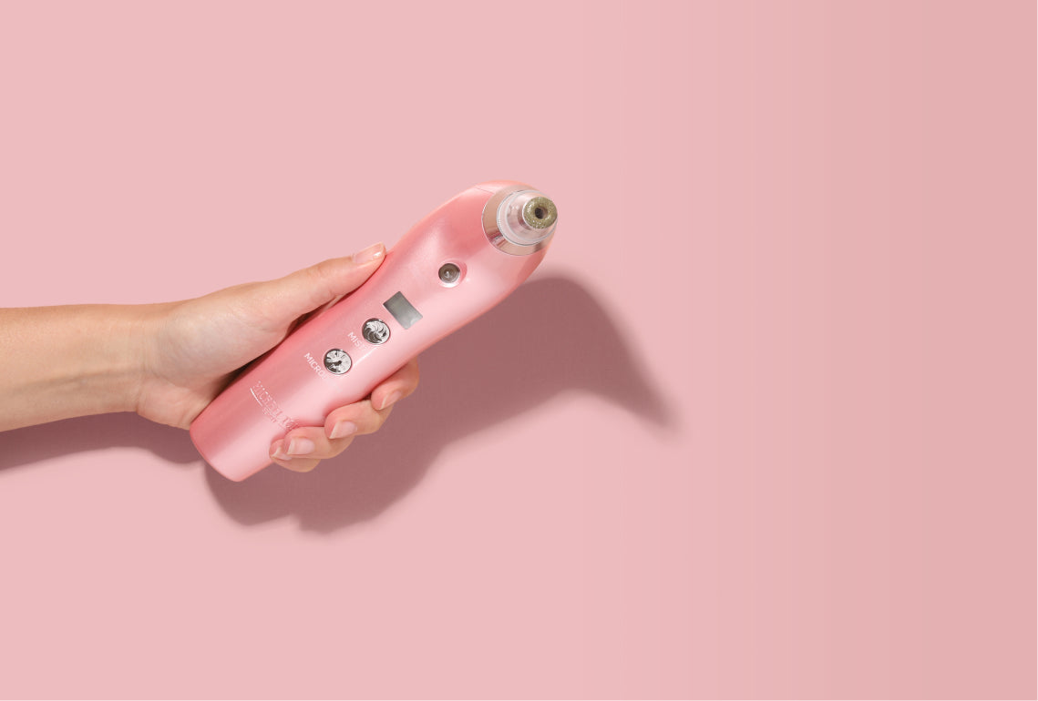 A woman's hand holding a pink electric shaver on a pink background.