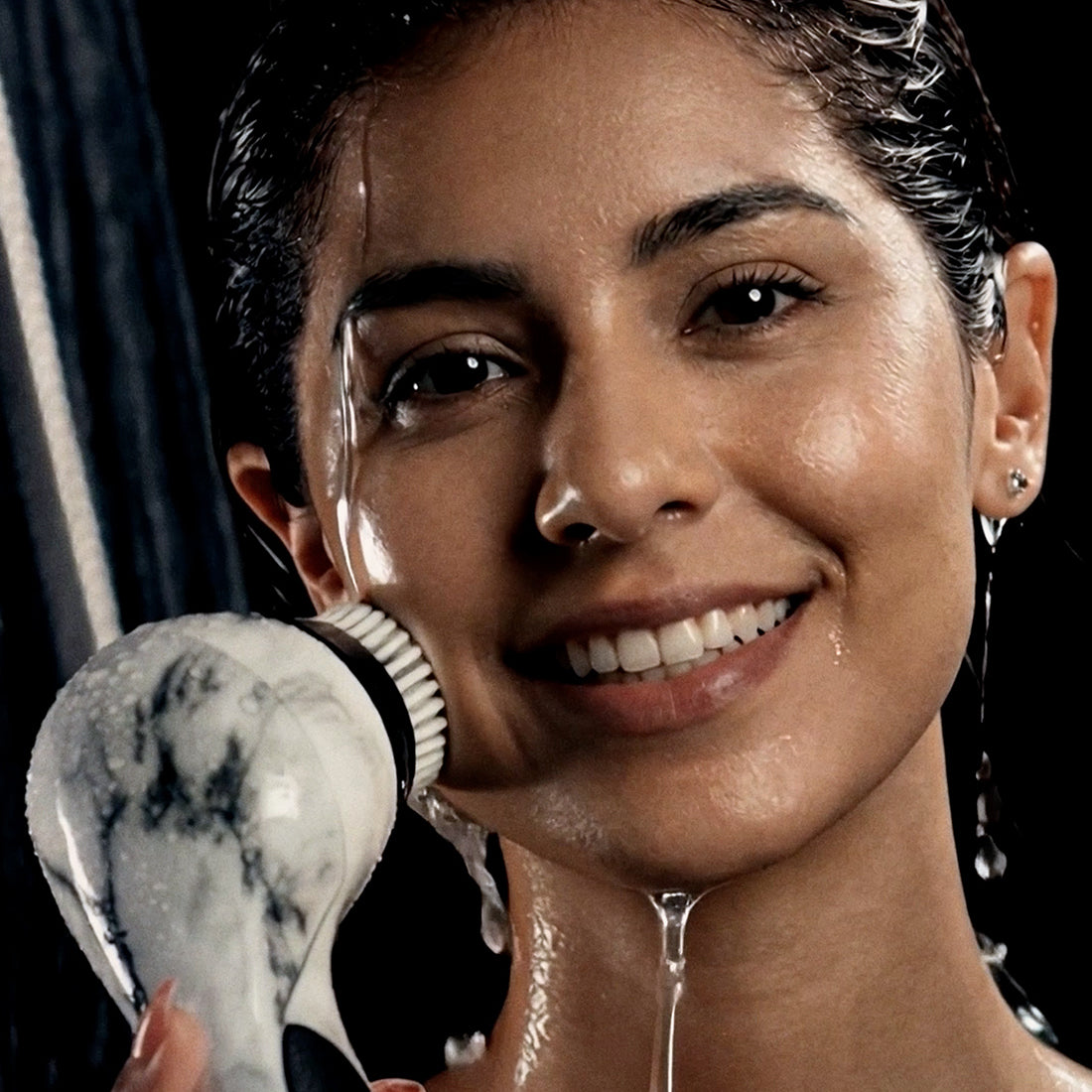 A woman smiling in the shower while using a Michael Todd Beauty Hydrojet handheld shower system.