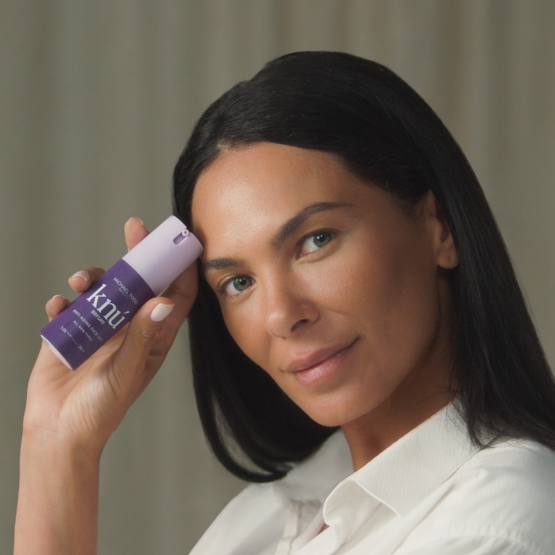 A woman holding a bottle of Knú Serum by Michael Todd Beauty.