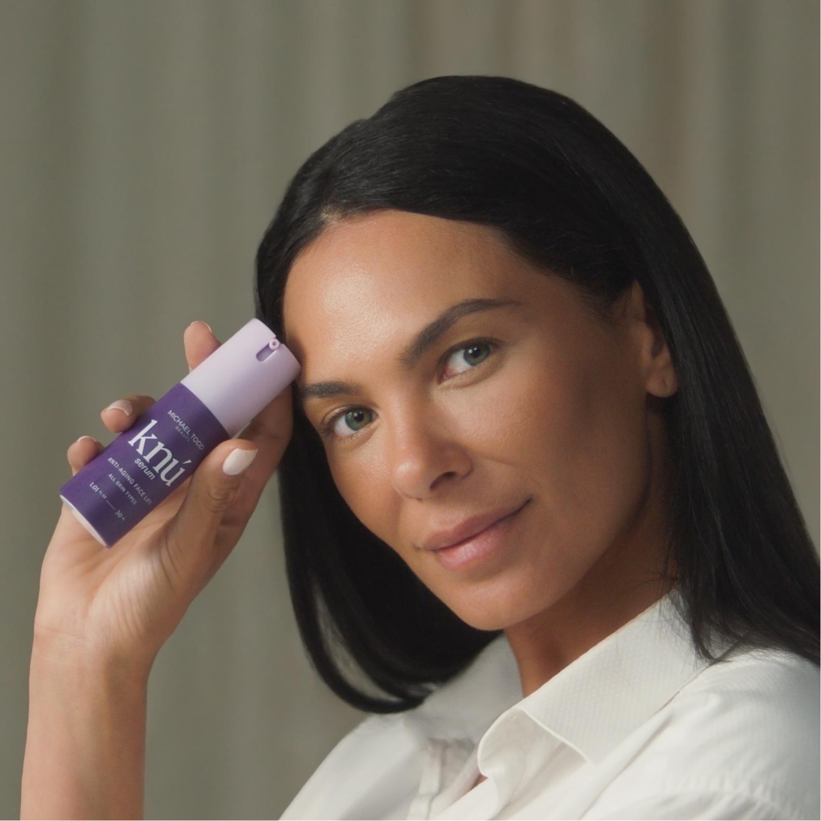 A woman is holding a Knú Ageless Duo rejuvenated serum lotion by Michael Todd Beauty.