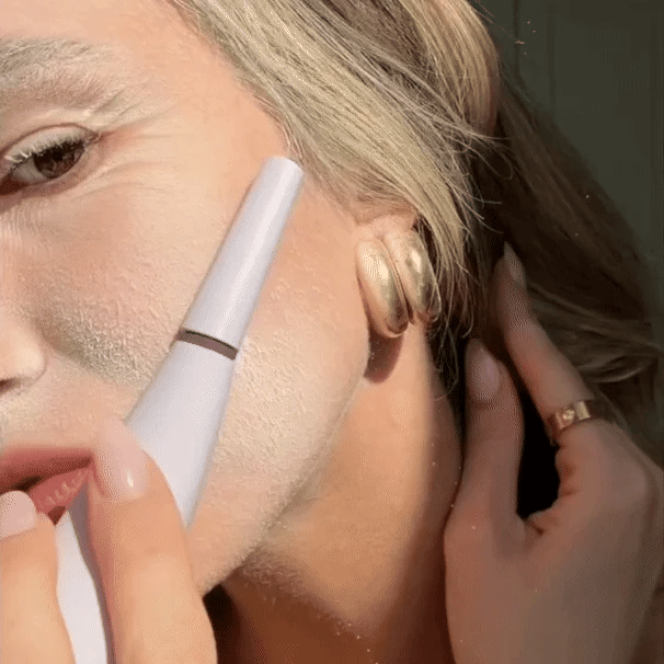 A person uses the Michael Todd Beauty Sonicsmooth Pro+ Starter Kit to apply a white substance to their cheek with an electronic skincare device, wearing a gold earring and ring.