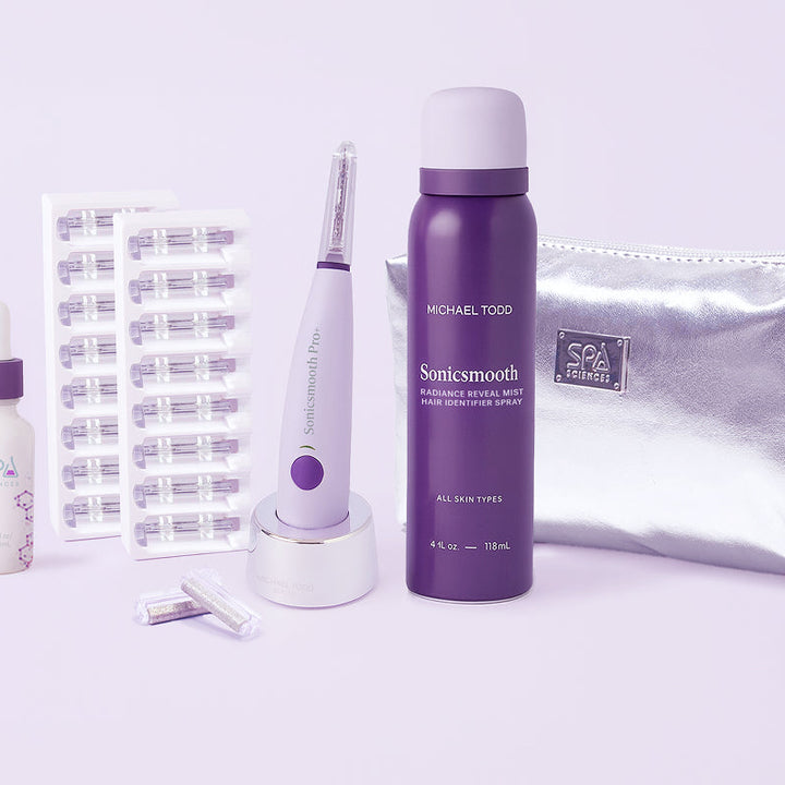 The Sonicsmooth Pro+ Complete Glow by Michael Todd Beauty includes a dropper bottle, capsule strips, electric device with stand, spray bottle, replacement heads, and a silver cosmetic bag, all displayed on a light background.