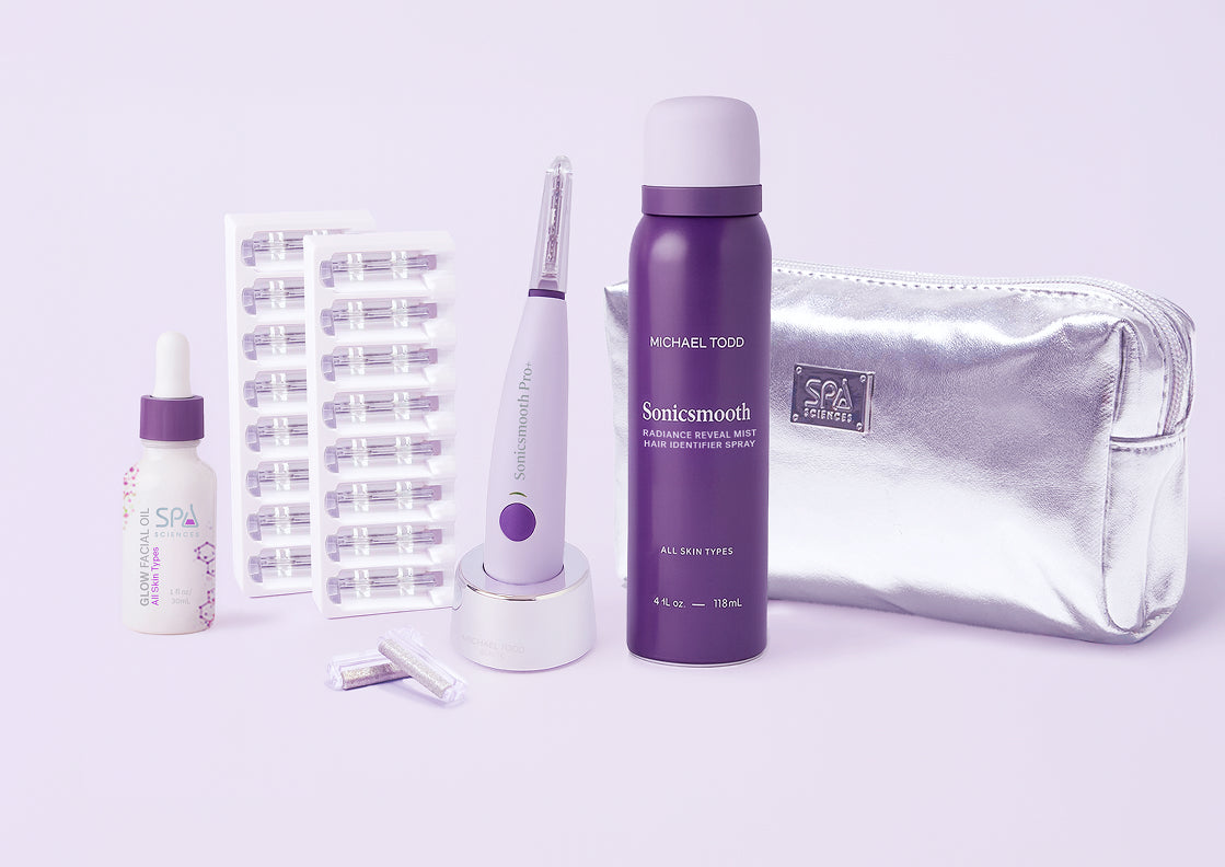 The Sonicsmooth Pro+ Complete Glow by Michael Todd Beauty includes a dropper bottle, capsule strips, electric device with stand, spray bottle, replacement heads, and a silver cosmetic bag, all displayed on a light background.