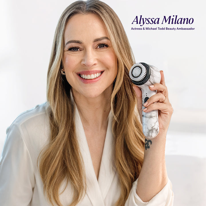 Alyssa Milano, Actress & Michael Todd Beauty Ambassador, smiles while holding the Soniclear sonic cleansing facial brush by Michael Todd Beauty near her face. Text reads: “Dermatologist recommended.”.