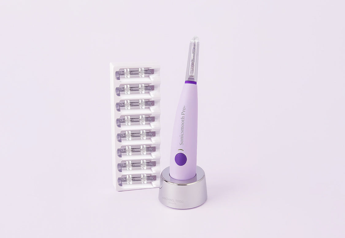 A purple Michael Todd Beauty Sonicsmooth Basic device stands on a charging base beside a tray with eight replacement heads, all set against a light background.